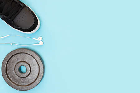 Sport and fitness concept. copyspace. place for text. Black sports shoes, headphones and dumbbell disk. blue background. flat lay. top view. Layout for design.の写真素材