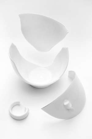 Broken white cup on a white background. vertical. Concept of carelessness. Mug was shattered into pieces.の写真素材