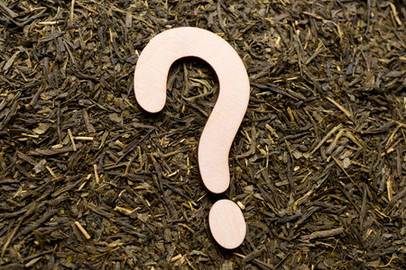 Wooden question mark on green tea leaves. Flat lay. Top view.