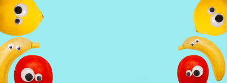 Blue banner with cheerful tomatoes, bananas and lemons. Place for text. copyspace. Vegetables and fruits with round plastic eyes. flat lay. top view.の写真素材