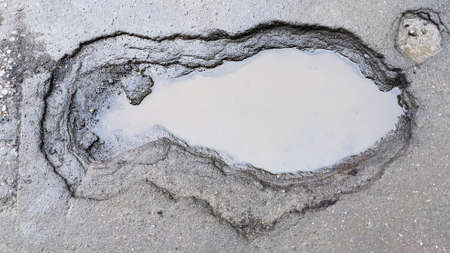 Damaged asphalt pavement. A hole in the road filled with water.