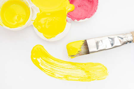 A smear, a stroke of yellow acrylic paint, a brush and a palette. White background.の写真素材