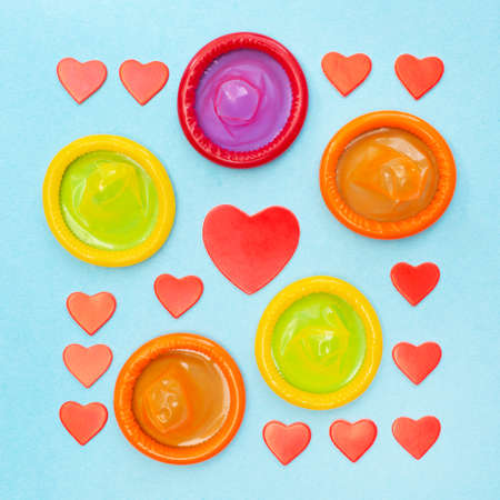 Condoms in different colors and many red hearts. Square. Safe or risky sex. Blue background....