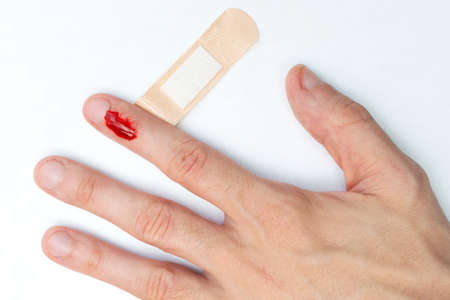 The man cut his finger and is bleeding. Accident. Top view. Providing first aid, sticking a medical plaster.の写真素材