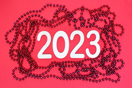 New Year 2023, numbers made of wood. Red background and red garlands. Flat lay. Top view.