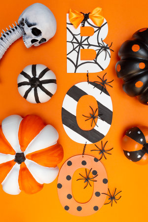 Boo text in halloween style. Pumpkins of different sizes and colors. Black spiders and white skull. Orange background. Halloween concept. Vertical. Flay lay. Top view.