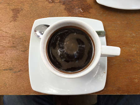 A cup of thick Lombok coffee in a white mug on a wooden table, with a silver spoon on the side
