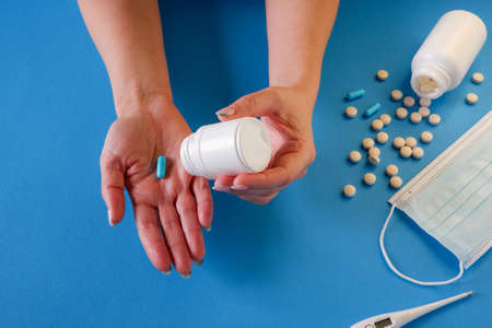 Medicine and healthcare concept. The woman removes the capsule from the container. Capsules, pills, medical mask on a blue background. Place for your text.の写真素材