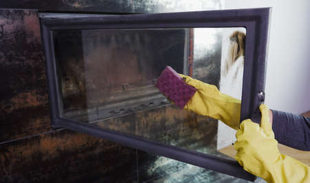 A woman in yellow gloves washes the glass of the fireplace. Homework daily winter routineの写真素材