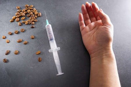 Grains of coffee and an injection syringe in female hands. Caffeine addiction concept.の写真素材
