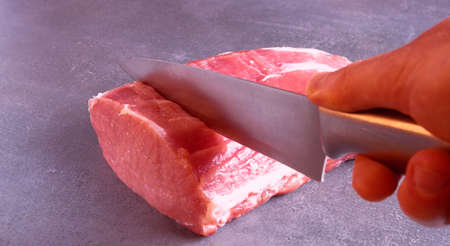 The chef is cutting fresh raw meat into steaks. Close-up on a gray background.の写真素材