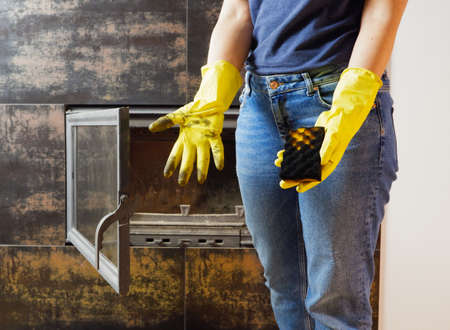 ? lose up of young woman in jeans, yellow gloves is cleaning the fireplace. Modern fireplace with glass.の写真素材