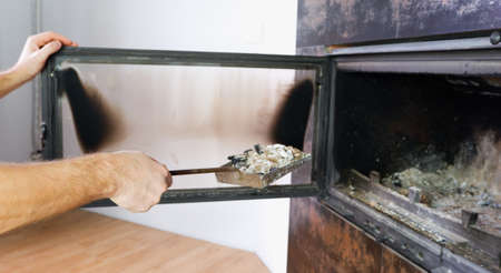 Fireplace cleaning. Man hand holds a shovel with ash.A hand collects ash from the fireplace on an old steel blade. Daily winter routineの写真素材