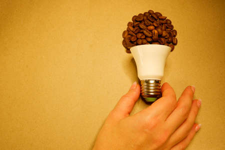 Female hand takes a light bulb from coffee beans on craft paperの写真素材