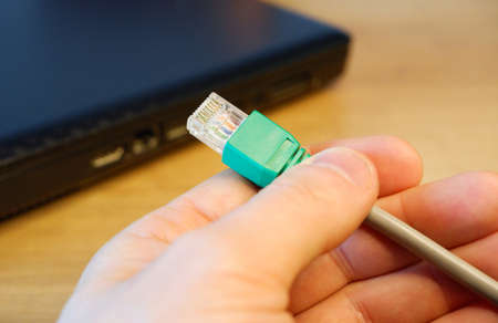 A woman's hand connects an RJ45 network connector to a laptop.の写真素材