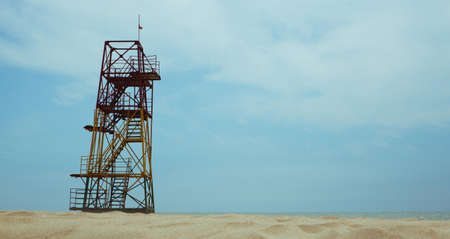 A metal observation tower of the beach rescue service, standing among the sand on the seashore against the blue sky.の写真素材