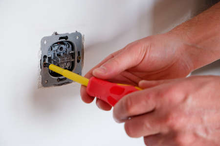 The electrician unscrews the switch with a screwdriver. Close-up on the hands. The routine work of an electrician. Checking contacts. Switch replacement.の写真素材