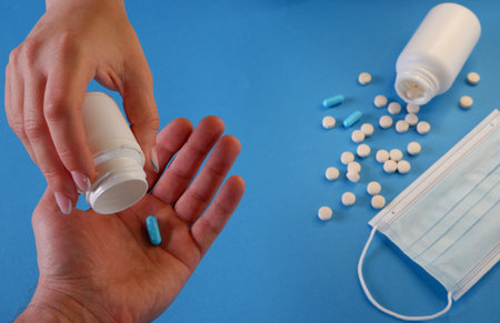 Medicine and healthcare concept. The woman gives the capsule to the man. Capsules, pills, medical mask on a blue background. Place for your text.の写真素材