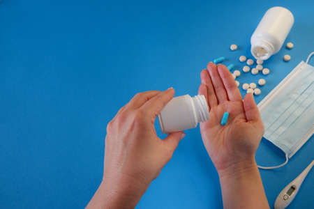 Medicine and healthcare concept. The woman removes the capsule from the container. Capsules, pills, medical mask on a blue background. Place for your text.の写真素材