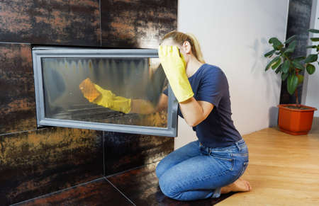 Homework. Young blonde woman in casual clothes cleans the fireplace.の写真素材