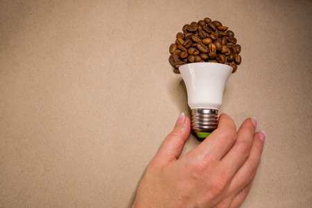 Female hand takes a light bulb from coffee beans on craft paperの写真素材