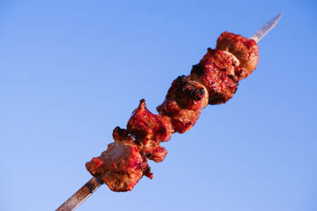 Juicy meat on skewers against the blue sky. Kebab of meat is fried on the grill.の写真素材