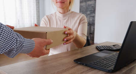 Remote work from home using a laptop. The courier made home delivery. A man hands over a cardboard...