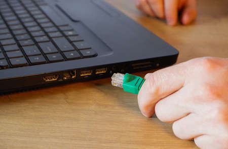 A man hand connects an RJ45 network connector to a laptop.の写真素材