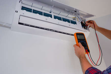Air conditioner repair and maintenance. The engineer diagnoses the electrical part of the indoor unit of the air conditioner with a measuring device.の写真素材