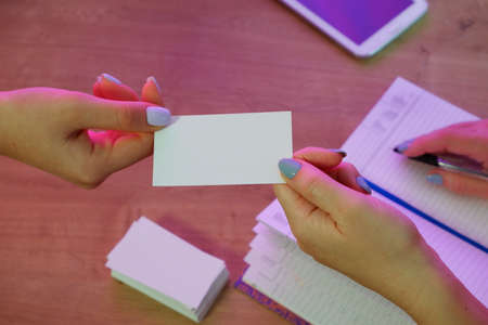 A woman gives a business card to a client. Notepad and tablet in the background on a wooden office table.の写真素材