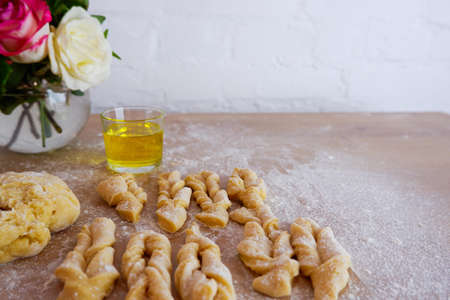 Making homemade cakes. Raw dough, butter, sugar, roses for making brushwood on a wooden tabletop. Concept on a white brick wall background. Homemade food during quarantine.の写真素材