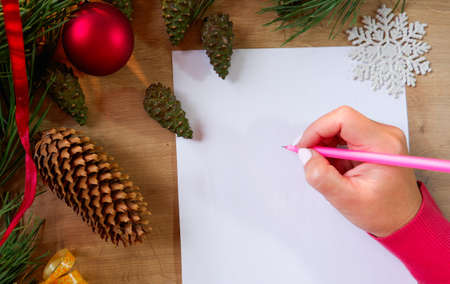 Young woman writes a New Year's greeting card or Christmas wish sheet on a white piece of paper. Christmas balls background.の写真素材