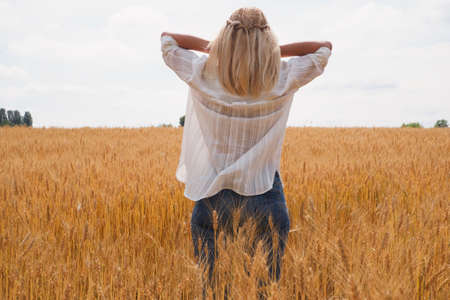 A young woman in a white shirt enjoys the moment among the golden wheat field against the blue sky....