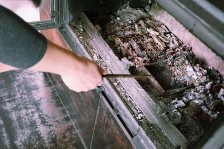 Fireplace cleaning. Woman hand holds a shovel with ash.A hand collects ash from the fireplace on an old steel blade. Daily winter routineの写真素材