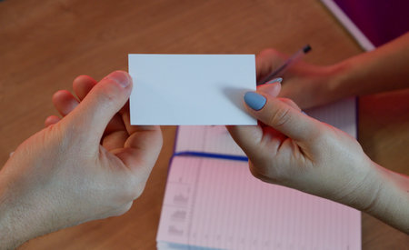 A woman gives a business card to a client. Notepad and tablet in the background on a wooden office table.の写真素材