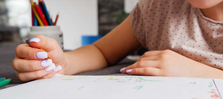 The girl makes a coloring with multi-colored pencils, close-up on hand. Home art hobby.