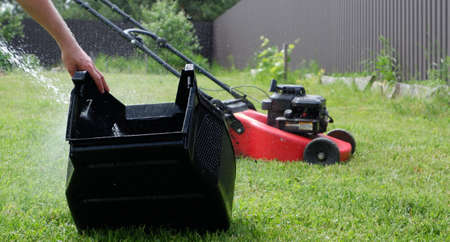 Washing the lawn mower's grass catcher with water. Splashes of water on a background of green grass....