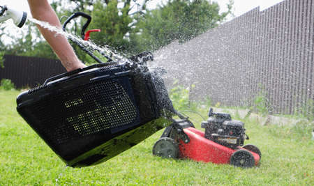 Washing the lawn mower's grass catcher with water. Splashes of water on a background of green grass....