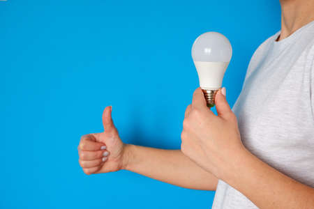 Concept of new idea and innovation with light bulbs. LED lamp in female hands on a blue background.