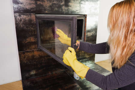 A woman in yellow gloves washes the glass of the fireplace. Homework daily winter routineの写真素材