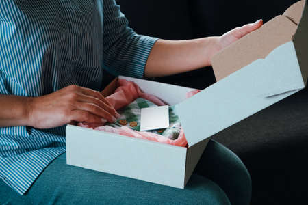 Delivery of clothes. A young woman opens a cardboard box with clothes from an online store. Blank...