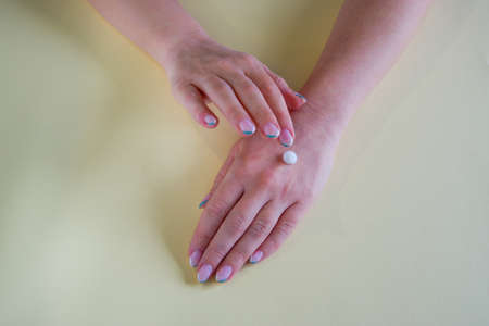 The girl applies a moisturizer to her hand. Close-up on the hands on a yellow backgroundの写真素材