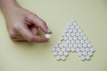 Female hands fold pills in the shape of a heart on a yellow background. Patient care.