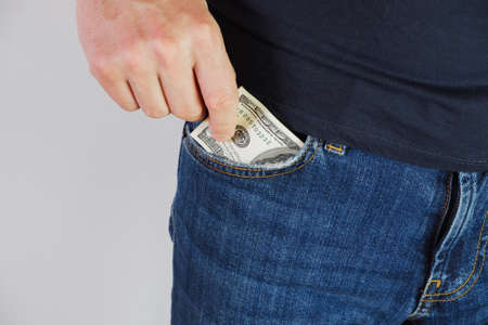The man pulls money out of the pocket of blue jeans. Close-up view of the hands. Place for your...