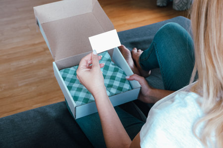 Online shopping. A woman examines a cardboard box with clothes from an online store. Blank business card place for text.の写真素材