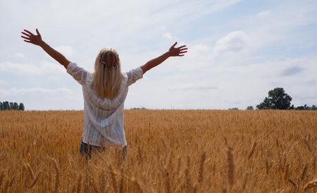 A young woman in a white shirt enjoys the moment among the golden wheat field against the blue sky....