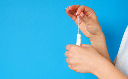 A girl with well-groomed hands holds a hygienic tampon. Close-up.