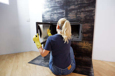 Homework. Young blonde woman in casual clothes cleans the fireplace.