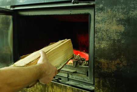 A man's hand puts wood in the burning fireplace. Modern closed fireplace with glass.の写真素材