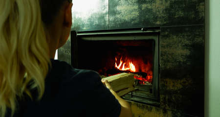 A woman's hand puts wood in the burning fireplace. Modern closed fireplace with glass.の写真素材